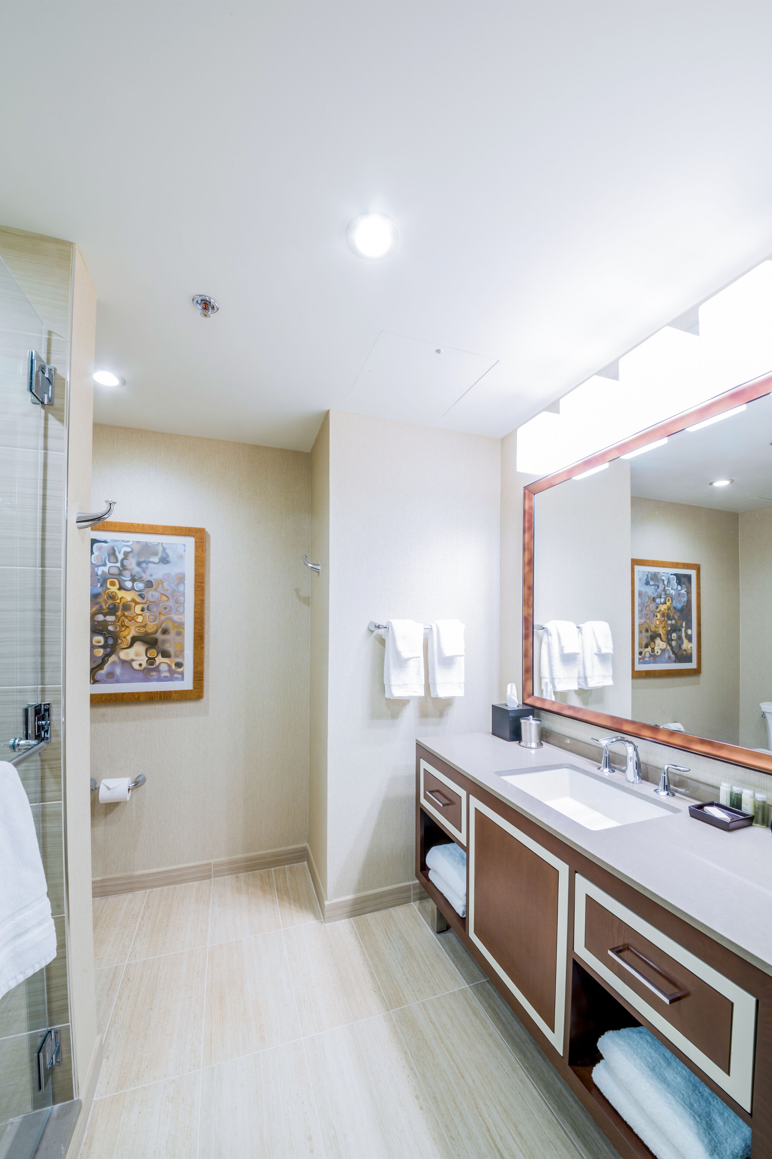A modern bathroom with a large mirror, two sinks, and a shower area.
