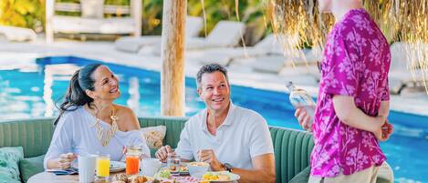 A poolside dining area with a table set for breakfast, overlooking a pool.
