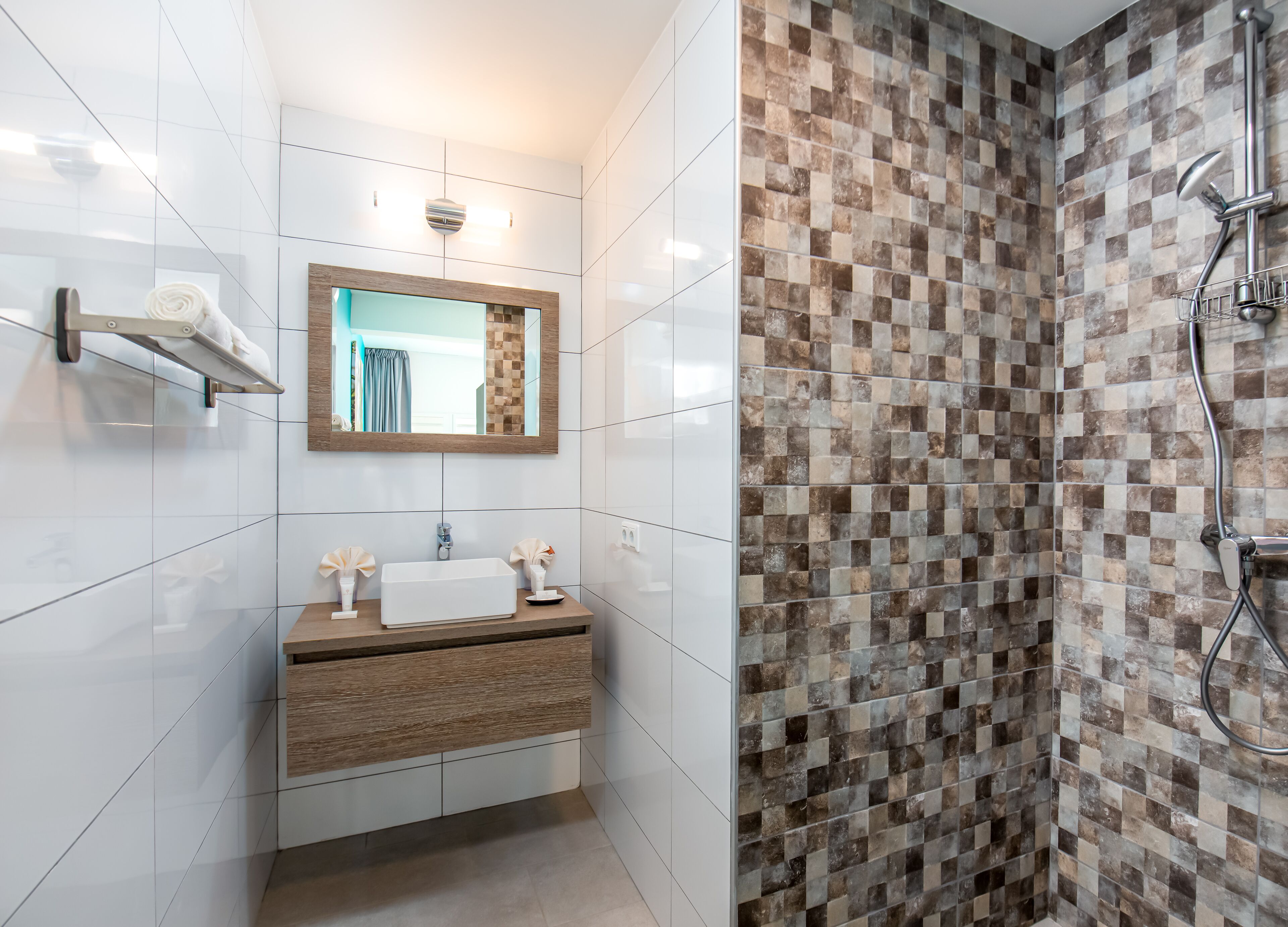 Een moderne badkamer met een wit wastafelmeubel, een spiegel, een douche met een betegelde muur in zwart-wit en een handdoekhouder.