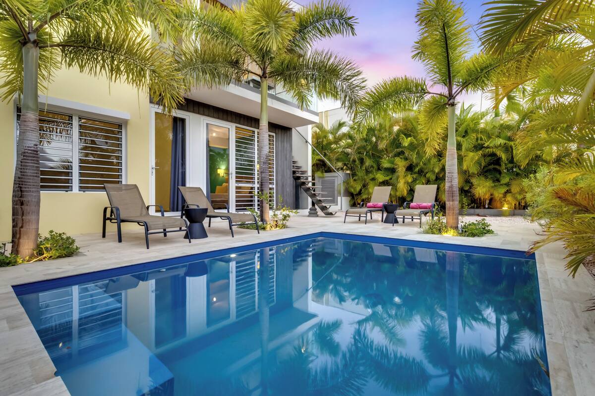 Uma casa moderna com piscina, área de estar externa e palmeiras.