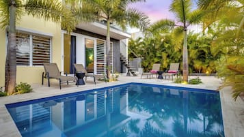 Et moderne hus med swimmingpool, udendørs møbler og palmer.
