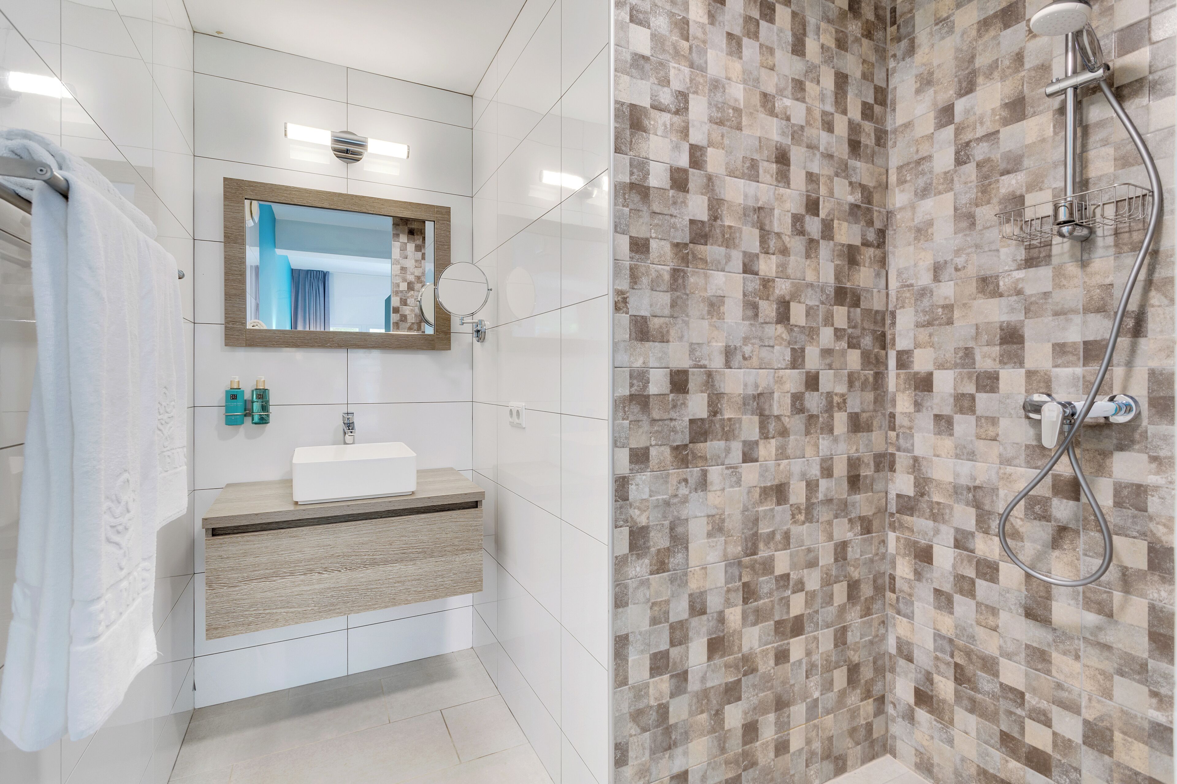 Une salle de bain moderne avec un lavabo blanc, un miroir et une zone de douche carrelée.