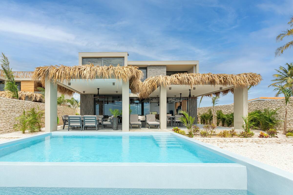 Um resort moderno com piscina, área de estar externa e estrutura com telhado de palha.