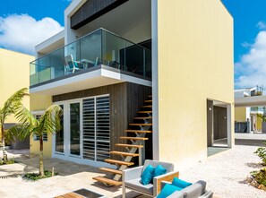 A modern two-story house with a glass balcony, a wooden staircase, and outdoor seating. - Delfins Residences (Kralendijk)