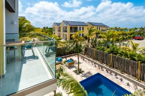 A modern building with a glass balcony overlooking a swimming pool and a landscaped garden. - Delfins Residences (Kralendijk)