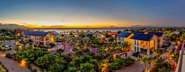 A resort with multiple buildings, a well-maintained garden, and a view of the ocean at sunset. - Delfins Residences (Kralendijk)