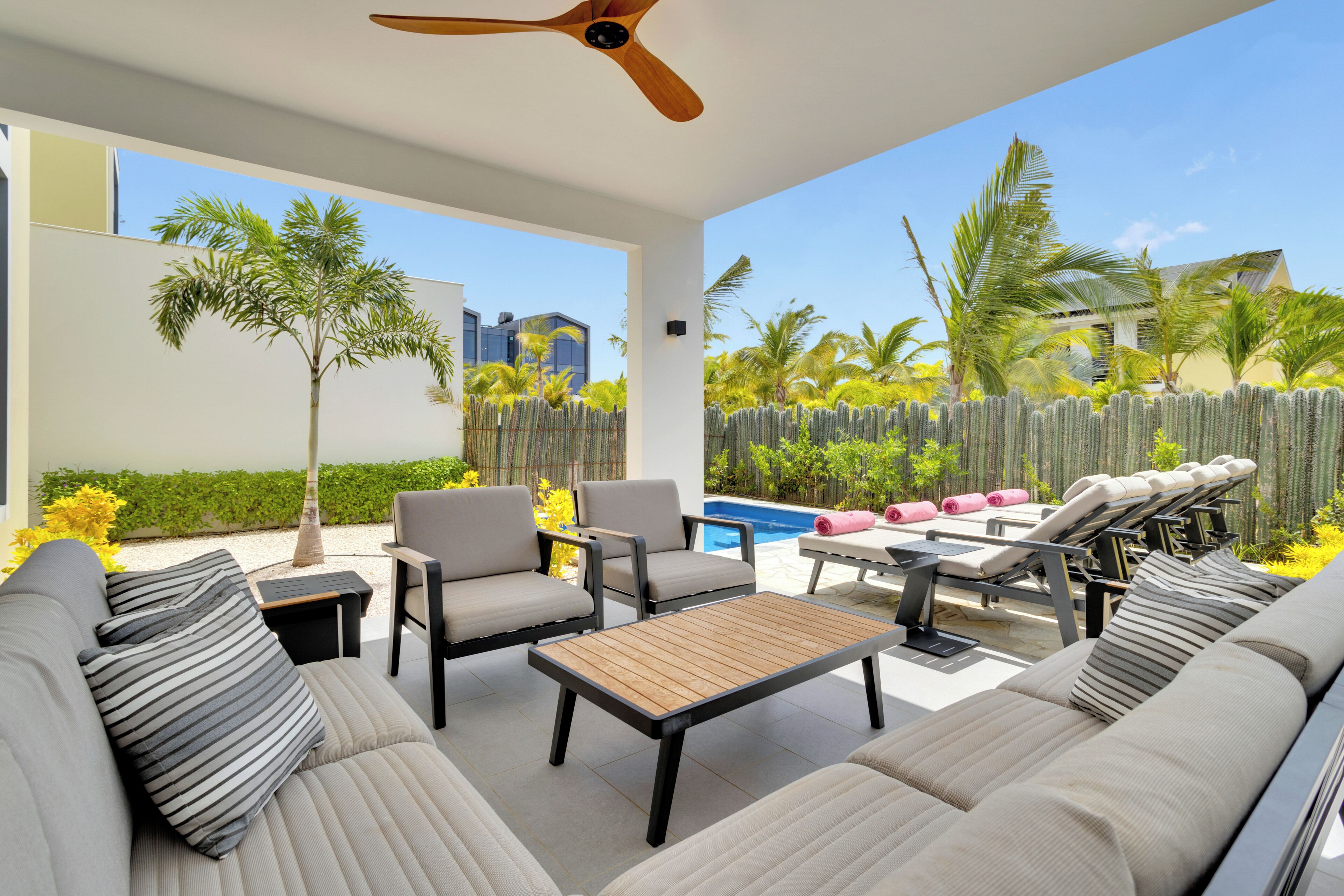 A modern outdoor living area with a pool, lounge chairs, and a ceiling fan.