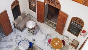 Un patio espacioso con techo de madera, un sofá, dos mesas redondas y una alfombra estampada.