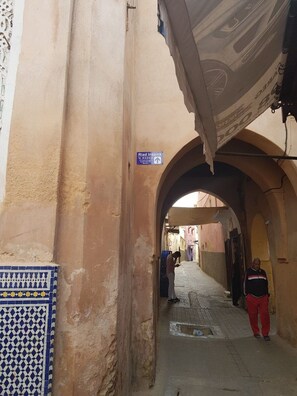 A narrow alleyway with a sign for 'Riad Inspira' and a tiled wall on the left.