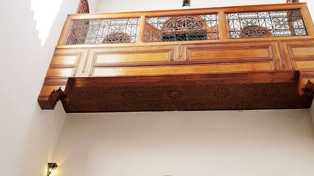 Interior arquitectónico tradicional con balcones de madera, barandillas de metal ornamentadas y una puerta central con un corte silueteado.