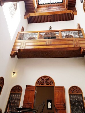 Interior arquitectónico tradicional con balcones de madera, barandillas de metal ornamentadas y una puerta central con un corte silueteado.