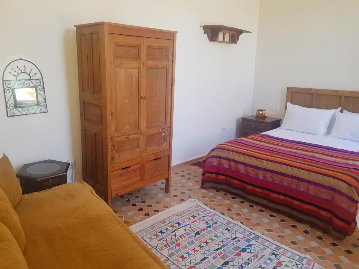 Un dormitorio con cama, un armario de madera, una mesita de noche con lámpara y una alfombra estampada.