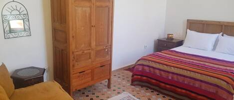 Un dormitorio con cama, un armario de madera, una mesita de noche con lámpara y una alfombra estampada.