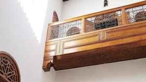 Un patio con un balcón de madera, puertas arqueadas y una mesa con sillas.