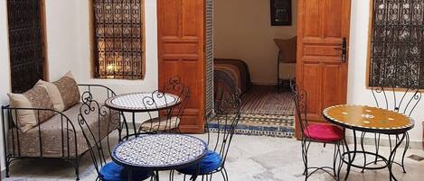 A cozy courtyard with a seating area featuring a sofa and two tables, surrounded by intricately designed wooden doors and windows.