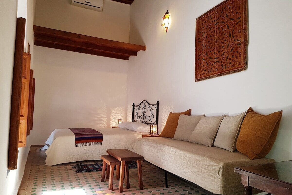 Uma sala de estar acolhedora com sofá, um banco de madeira, piso estampado e um objeto decorativo na parede.