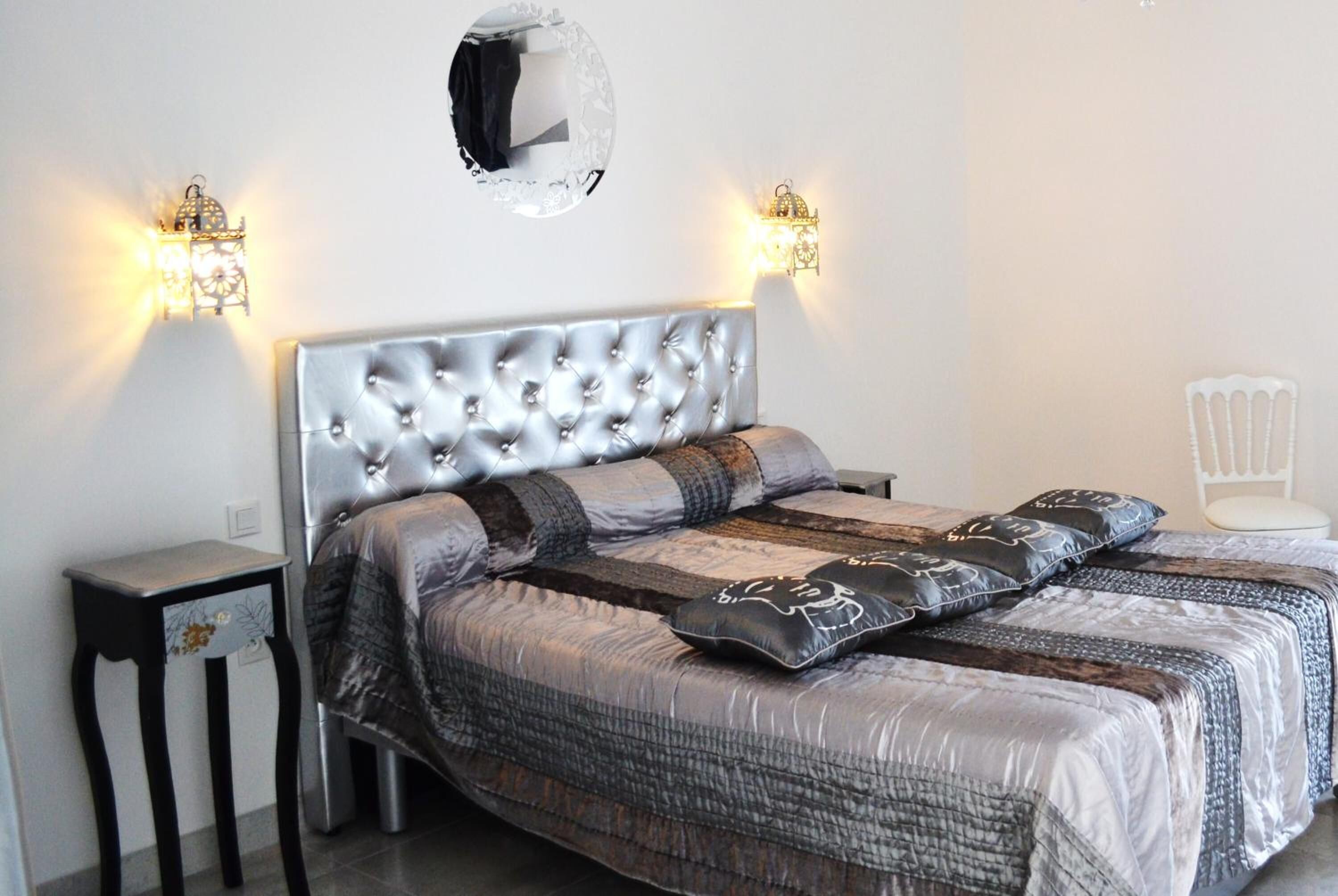 Een slaapkamer met een gestoffeerd hoofdeinde, een bed met beddengoed met een patroon, twee nachtkastjes en wandlampen.