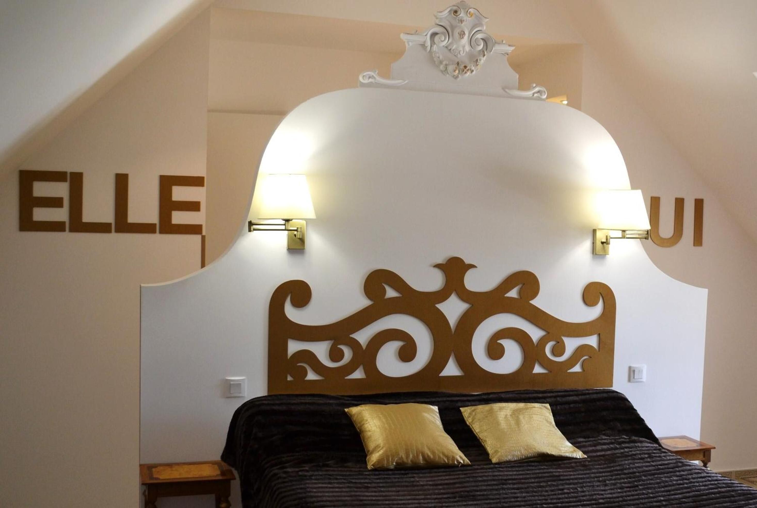 A bedroom with a decorative headboard, two bedside lamps, and a bed with two pillows.