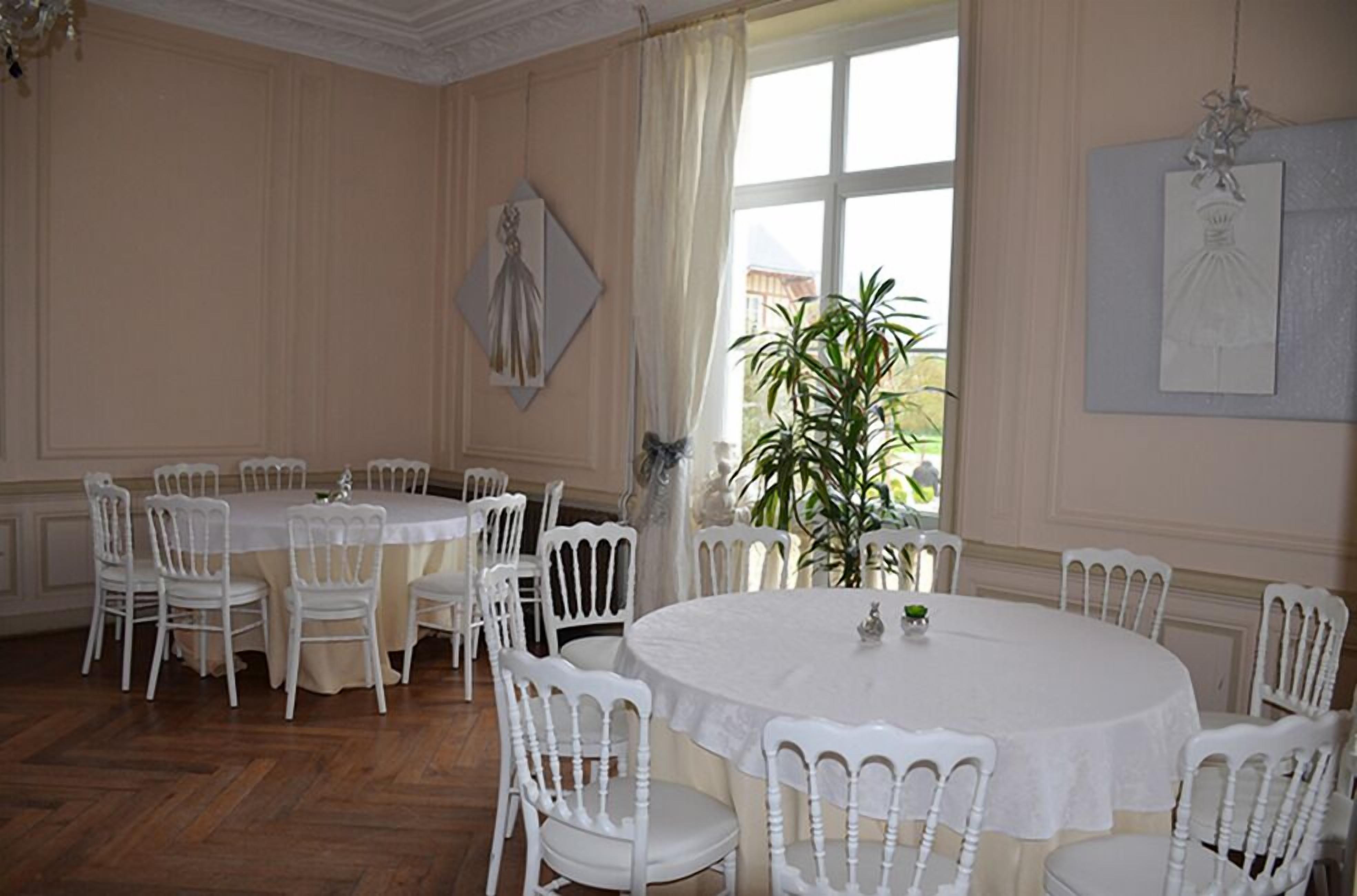 A dining room with a round table and white chairs, a potted plant, and artwork on the walls.