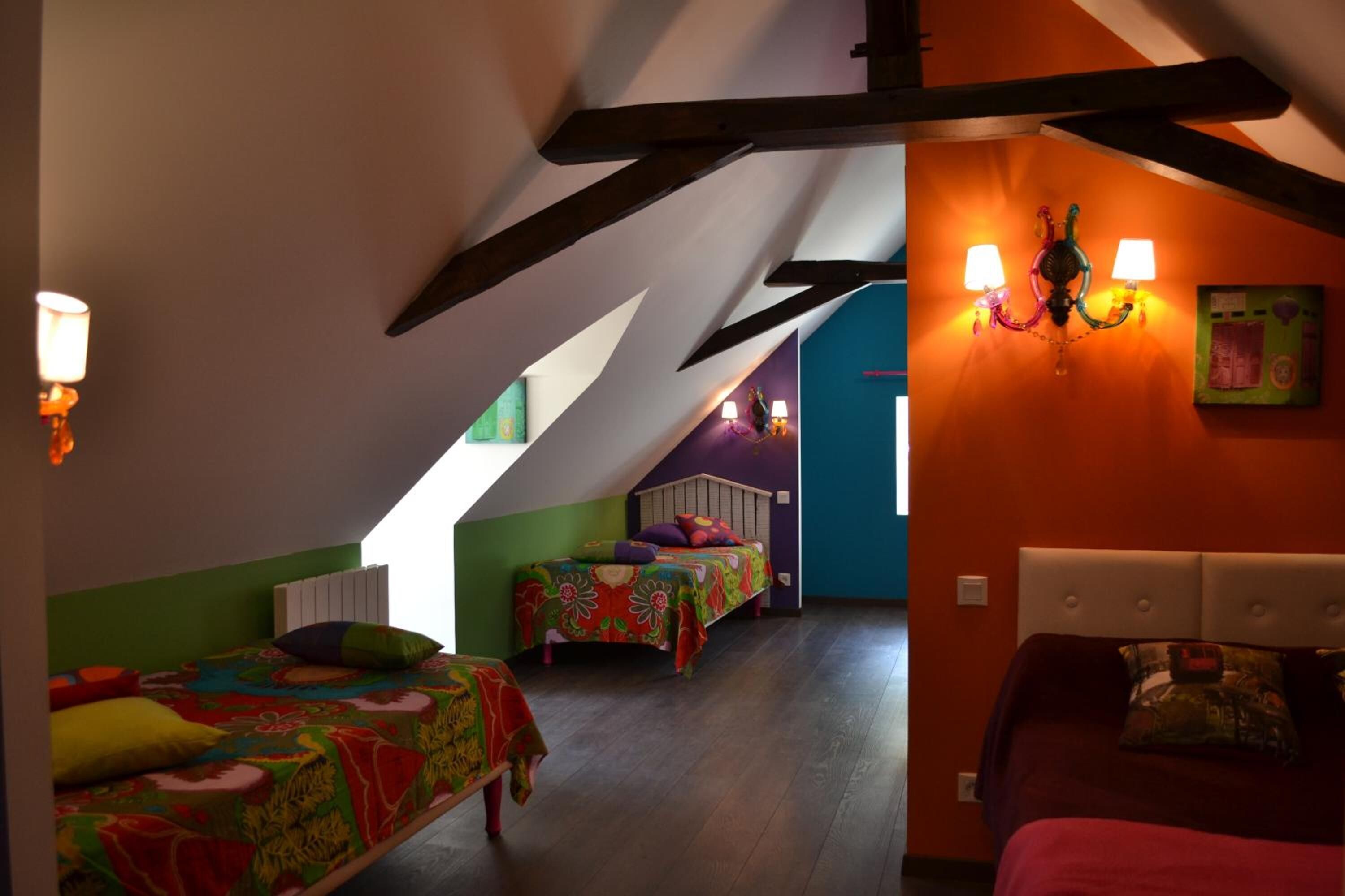 A room with two beds, a sloped ceiling, and a wall-mounted lamp.