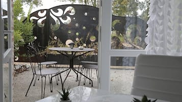 Un patio con una mesa redonda y sillas, una verja metálica decorativa, y vistas a árboles y un ciervo.