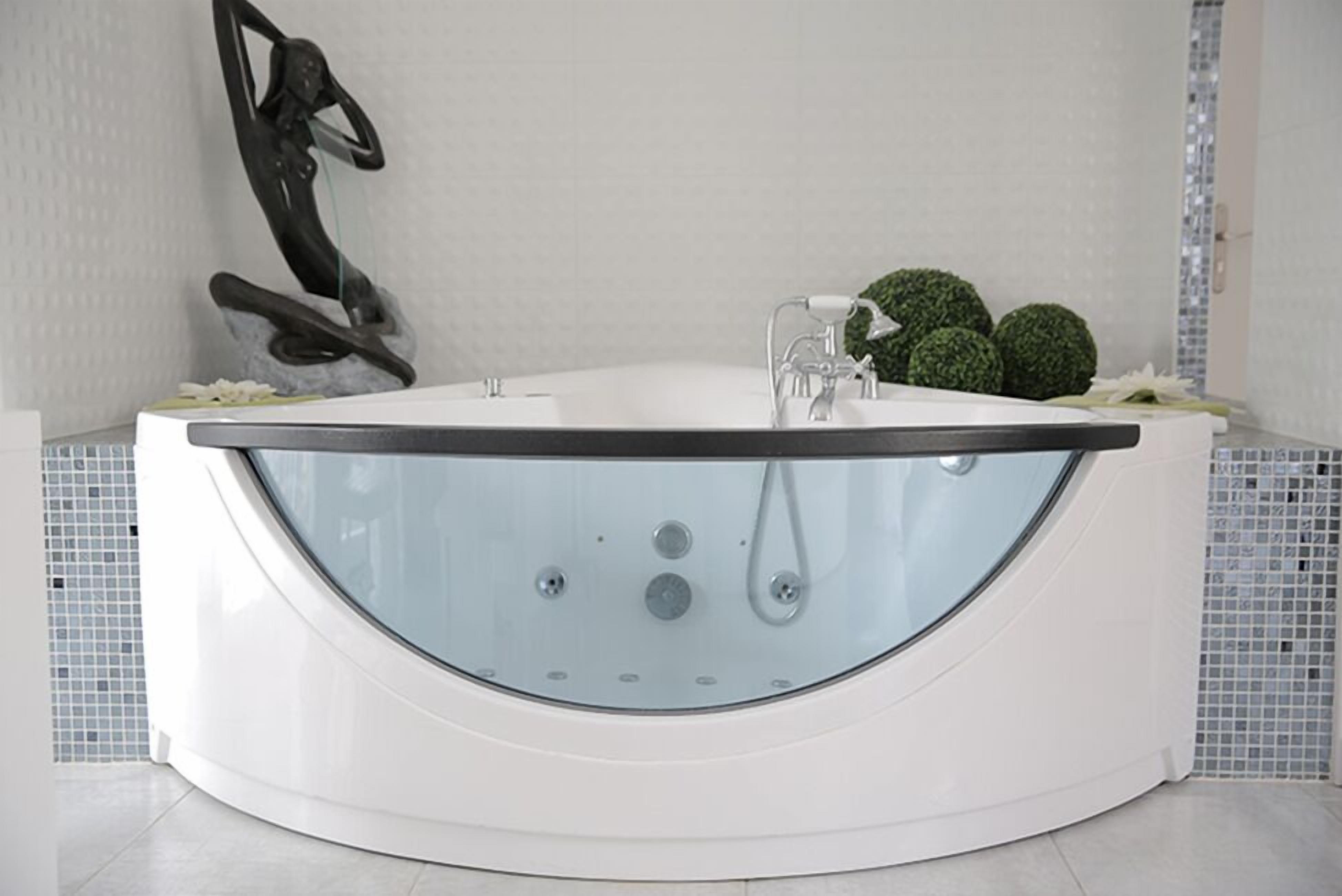 A modern, freestanding bathtub with a glass front, positioned in a bathroom with a tiled backsplash and a decorative sculpture.