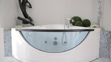 A modern, freestanding bathtub with a glass front, positioned in a bathroom with a tiled backsplash and a decorative sculpture.