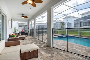 A covered patio area with wicker furniture, a ceiling fan, and a view of a swimming pool and houses in the background. - Champions Gate 9026 (Davenport)
