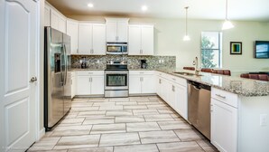 A modern kitchen with white cabinets, stainless steel appliances, granite countertops, and a herringbone floor pattern. - Champions Gate 1403 (Davenport)