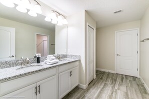 A bathroom with a granite countertop, white cabinets, a large mirror, and a shower area. - Champions Gate 1403 (Davenport)