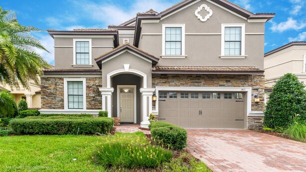 A two-story house with a stone facade, a garage, and a well-maintained front yard with hedges and a palm tree. - Champions Gate 1403 (Davenport)