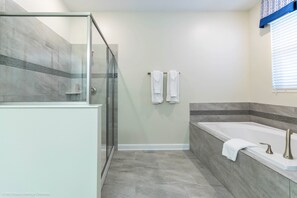 A bathroom with a glass-enclosed shower, a bathtub, and a towel rack. - Champions Gate 1686 (Davenport)