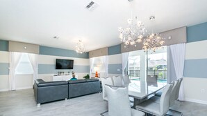 A modern living room with a grey sofa, a dining table with chairs, a TV, and a chandelier. - Champions Gate 1686 (Davenport)