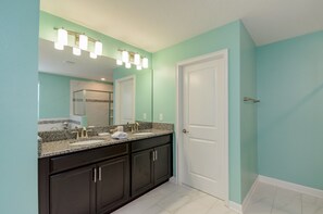 A bathroom with teal walls, a white door, dark cabinets, a granite countertop, a sink, a mirror, and a shower area. - Champions Gate 9037 (Davenport)