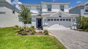 A two-story residential house with a white exterior, a blue front door, and a garage. - Champions Gate 9037 (Davenport)