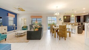 A modern open-plan living and dining area with a kitchen, featuring a ceiling fan, a dining table with chairs, and a kitchen island. - Champions Gate 9037 (Davenport)
