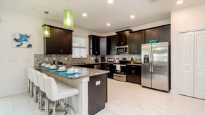 A modern kitchen with dark cabinets, stainless steel appliances, and a central island with bar stools. - Champions Gate 9037 (Davenport)