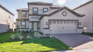 A two-story residential building with a garage, a front door, and a small garden area. - Champions Gate 1514 (Davenport)