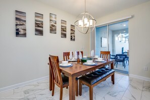 Uma área de refeições com mesa de madeira posta para seis pessoas, seis cadeiras e um banco. Quatro obras de arte emolduradas na parede.