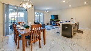 A modern kitchen with a central island, a dining area with wooden chairs, and a large sliding glass door leading to an outdoor patio. - Champions Gate 8953 (Davenport)