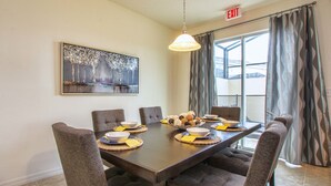 A dining area with a dark wooden table, six upholstered chairs, and a painting on the wall.