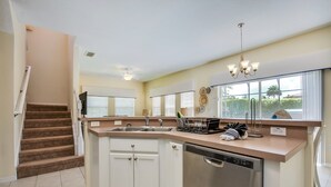 A kitchen with white cabinets, a dishwasher, a countertop with a sink, and a window with blinds. - Bella Vida 4550 (Kissimmee)