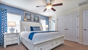 A bedroom with a white bed, a nightstand, a ceiling fan, and a door. - Bella Vida 4550 (Kissimmee)