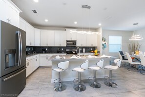 Uma cozinha moderna com armários brancos, eletrodomésticos de aço inoxidável e uma ilha central com banquetas.
