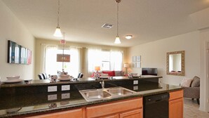 A kitchen with granite countertops, a dishwasher, wooden cabinets, pendant lighting, and a window with curtains.