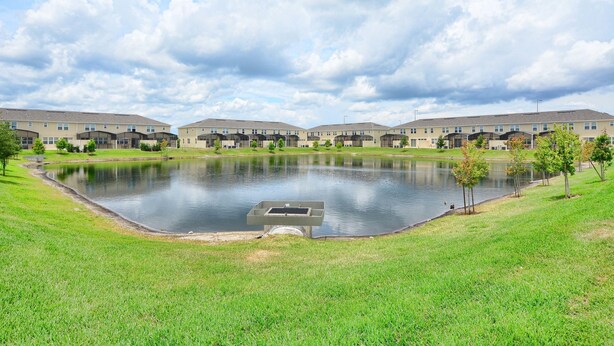 A residential complex with a central pond, surrounded by well-maintained lawns and small trees.