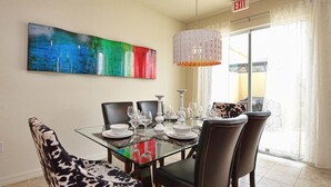 A dining area with a glass table, leather chairs, and a colorful abstract painting on the wall.