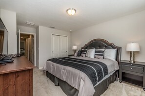 A bedroom with a large bed, bedside tables with lamps, a wooden desk, and a door leading to another room. - Compass Bay 5153 (Kissimmee)