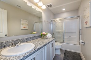 A modern bathroom with a granite countertop sink, a glass shower enclosure, and a toilet. - Compass Bay 5153 (Kissimmee)