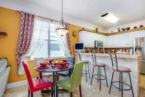 Une cuisine moderne avec des meubles blancs, un coin repas avec des chaises rouges et vertes, et un bar avec des tabourets.